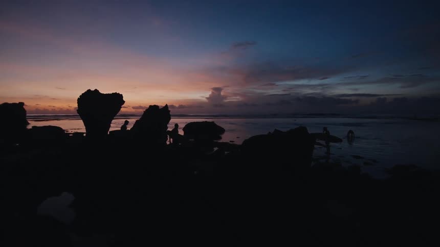 Silhouetted surfers enjoy the last light of the day on a rocky beach with a beautiful sunset sky