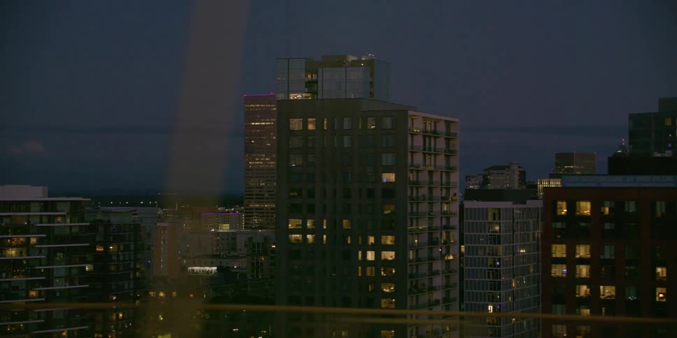 A slow pan across a modern city skyline at night, with illuminated skyscrapers and apartment buildings