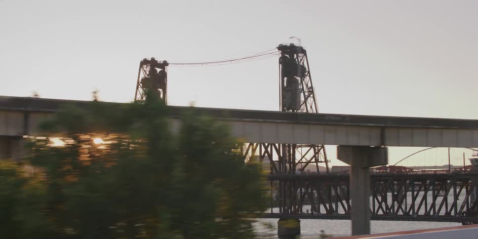 A slow-motion driving shot passing the historic Steel Bridge in Portland, Oregon, beautifully silhouetted by the golden hour sun