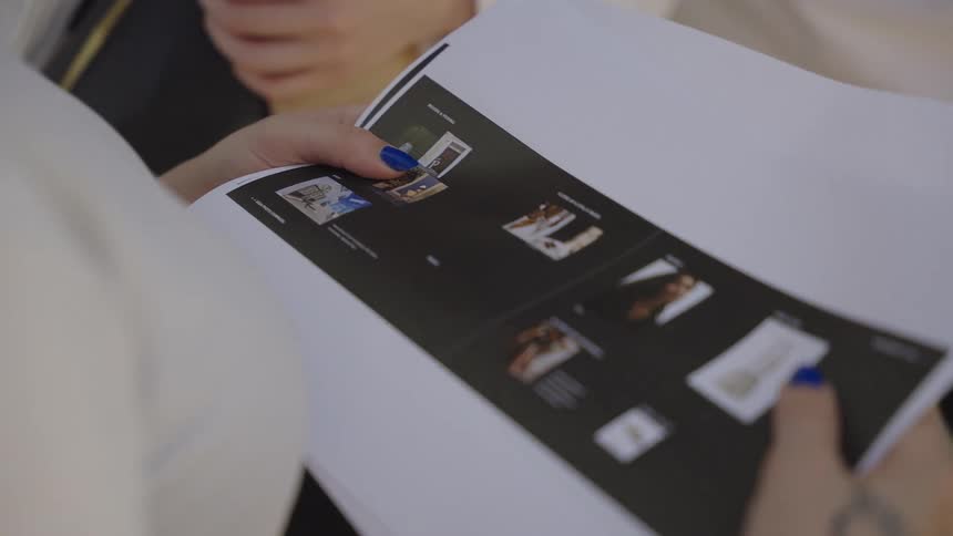 A close-up of a woman's hands with blue nail polish looking over a printed document with images