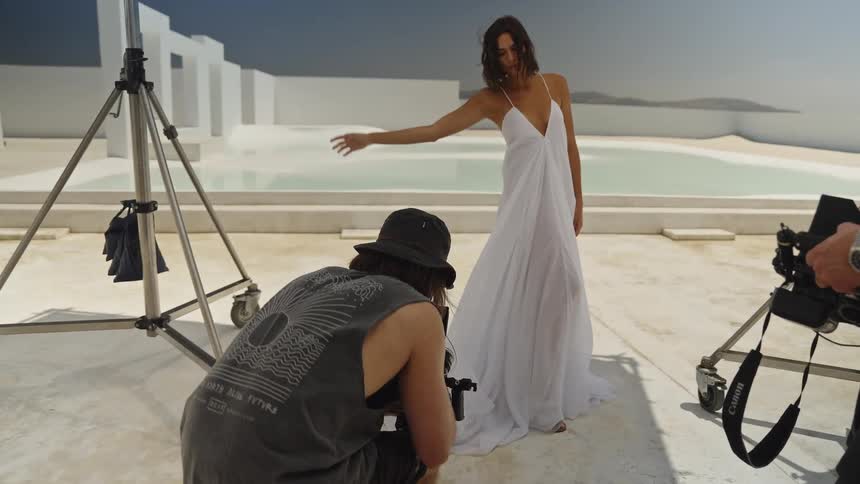 Behind the scenes of a fashion video shoot as a photographer films a model in a white dress at a modern, minimalist location