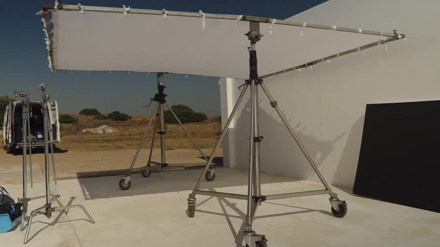 Behind the scenes on a sunny outdoor film set with a large butterfly scrim and other professional lighting equipment