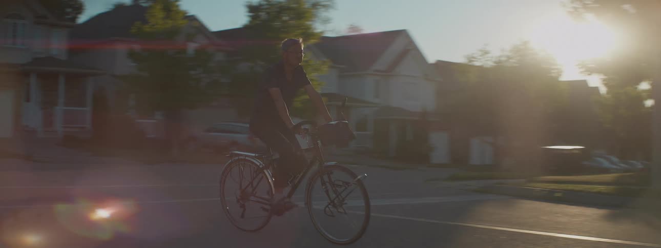 Tracking shot of a middle-aged man enjoying a leisurely bike ride through a suburban neighborhood during golden hour