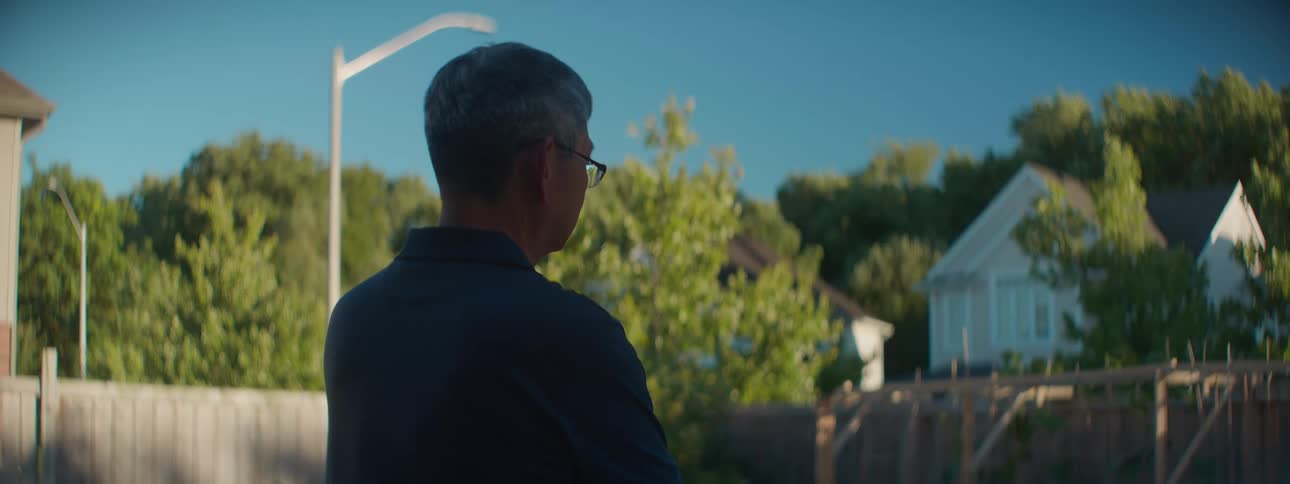 A pensive senior man looks out over his suburban neighborhood from his backyard on a sunny day