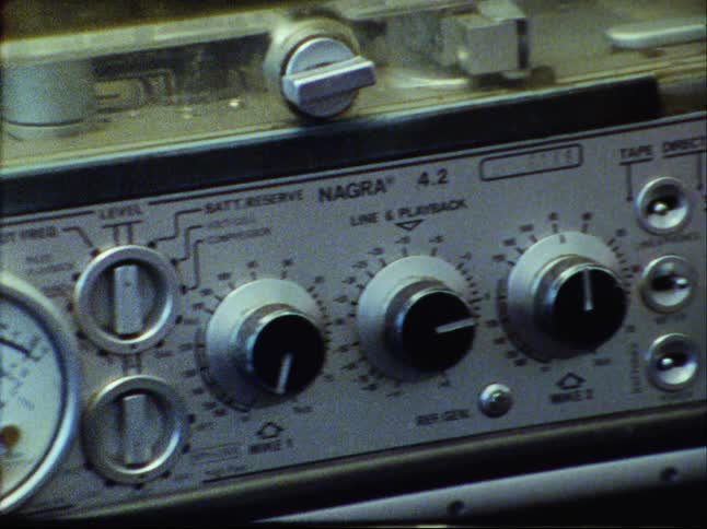 Close-up pan across the dials and controls of a vintage Nagra 4.2 audio tape recorder, ending with a film burn effect