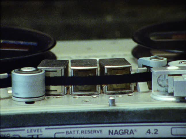 Close-up of a vintage reel-to-reel tape recorder playing, with a grainy Super 8 film aesthetic