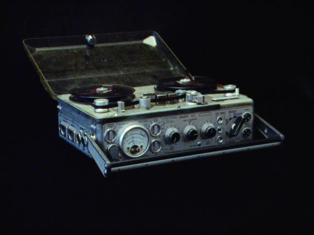 Vintage Nagra reel-to-reel tape recorder with spinning tapes isolated on a black background