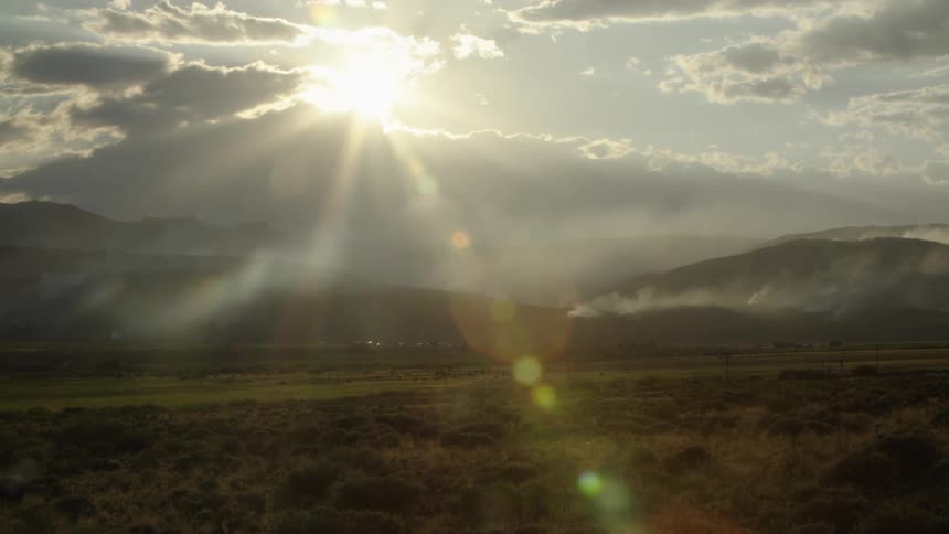 Sunbeams shine through the clouds onto a smoky mountain valley landscape at dusk