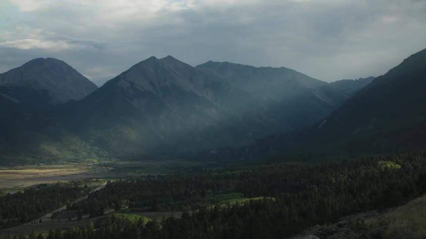 Dramatic sunbeams illuminate a vast, forested mountain valley under a cloudy sky