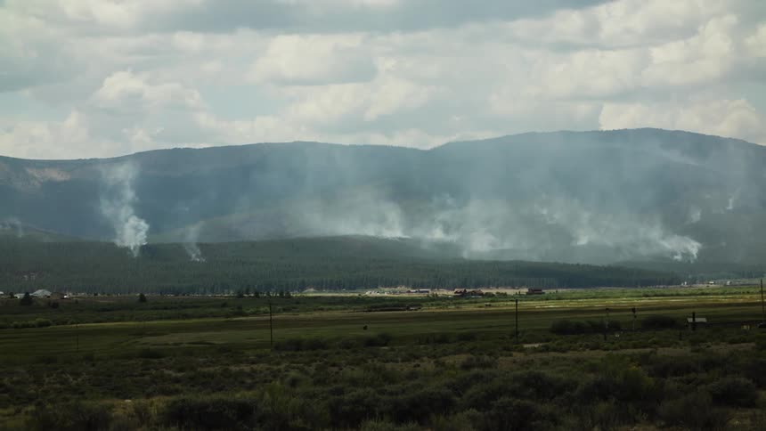 Smoke rises from multiple points across a forested mountain range during a wildfire