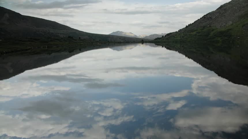 A serene mountain lake perfectly mirrors the cloudy sky and surrounding peaks
