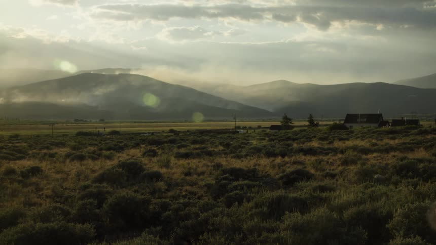Sun rays pierce through the clouds over a hazy mountain valley where smoke from a distant wildfire rises into the sky
