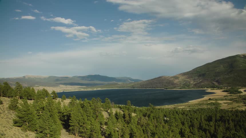 A serene mountain lake is surrounded by a dense evergreen forest on a partly cloudy day