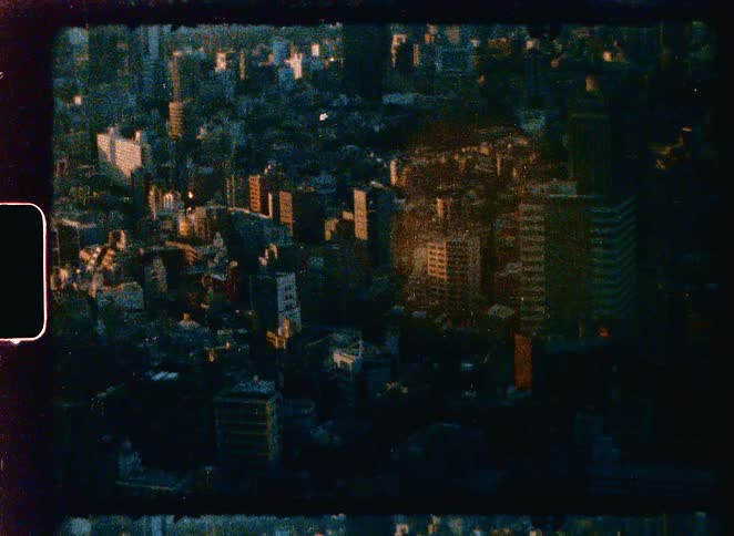 A grainy, vintage super 8mm film shot of a dense cityscape from a high angle at golden hour