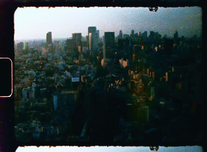 A vintage 8mm film captures an aerial view of a sprawling city skyline during a hazy sunrise
