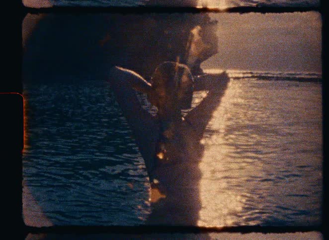 Grainy vintage footage shows a woman's silhouette as she relaxes in the warm ocean water at sunset