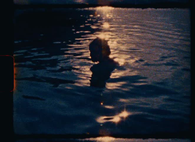 A nostalgic, vintage-style shot shows the silhouette of a person swimming in the water as the golden sunset reflects on the surface