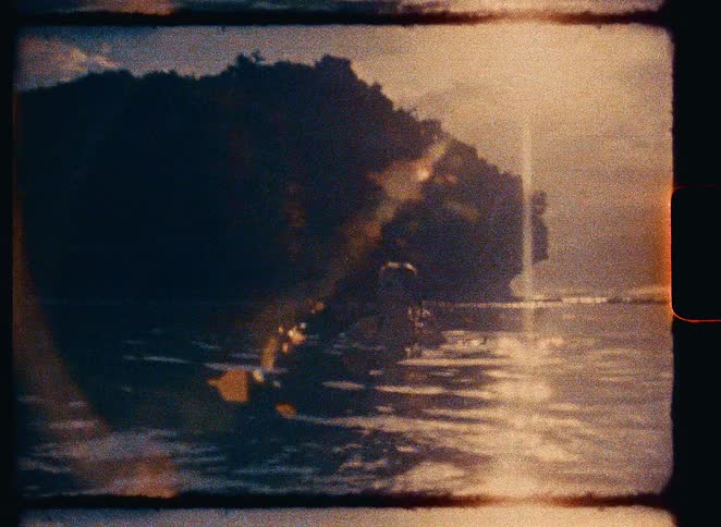 Vintage Super 8mm film of a lone surfer sitting on her board, waiting for waves in the warm glow of sunset