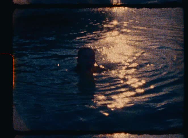 A person struggles in dark water as their hands emerge from the surface, captured on vintage super 8mm film