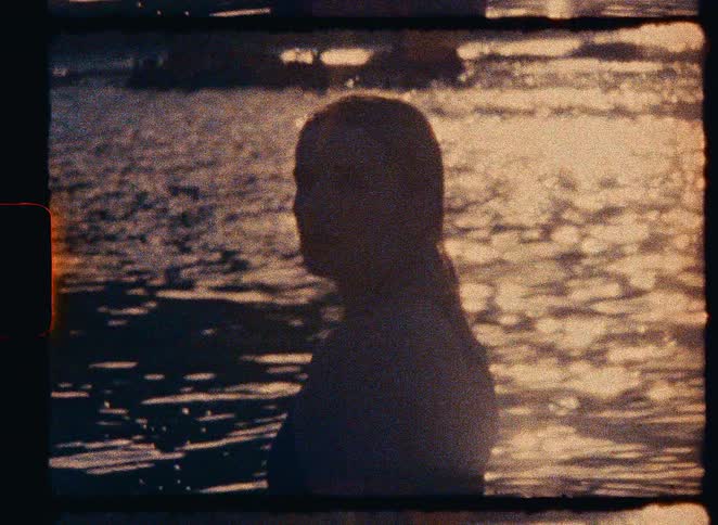 Vintage 8mm film captures the silhouette of a woman in the water as the sunset reflects off the surface