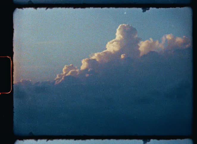 A vintage, grainy film shot of sunlit clouds against a deep blue sky