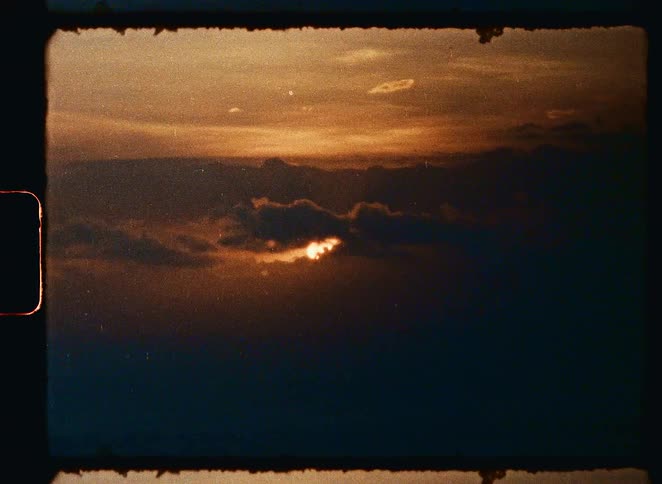 Super 8mm vintage footage shows the sun shining through dark clouds at sunset