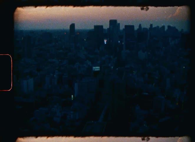 Vintage 8mm film captures a dark and moody aerial view of a sprawling city skyline at dusk