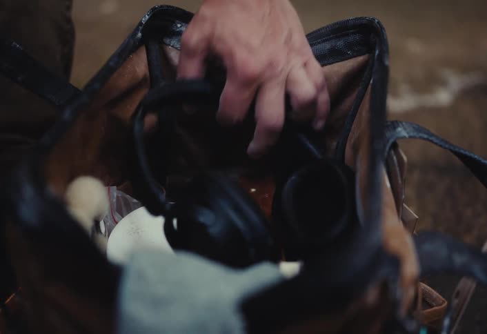 Close-up of a worker reaching into a dirty work bag and pulling out a pair of black headphones