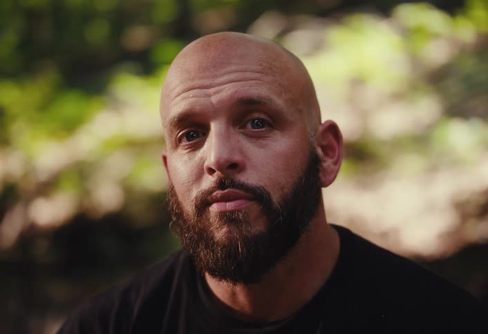 Close up portrait of a pensive bald man with a beard looking into the camera while outdoors