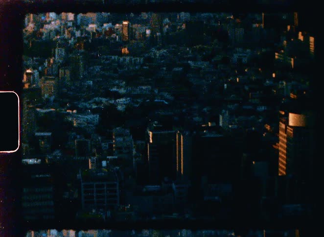Vintage 8mm footage provides an aerial perspective of a dense cityscape basking in the warm light of sunrise or sunset