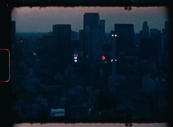 Super 8 footage shows a grainy, dark cityscape with silhouetted buildings and flickering neon lights at dusk