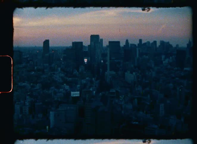 Vintage 8mm footage captures the moody, sprawling cityscape of Tokyo at dusk with a hazy sunset on the horizon