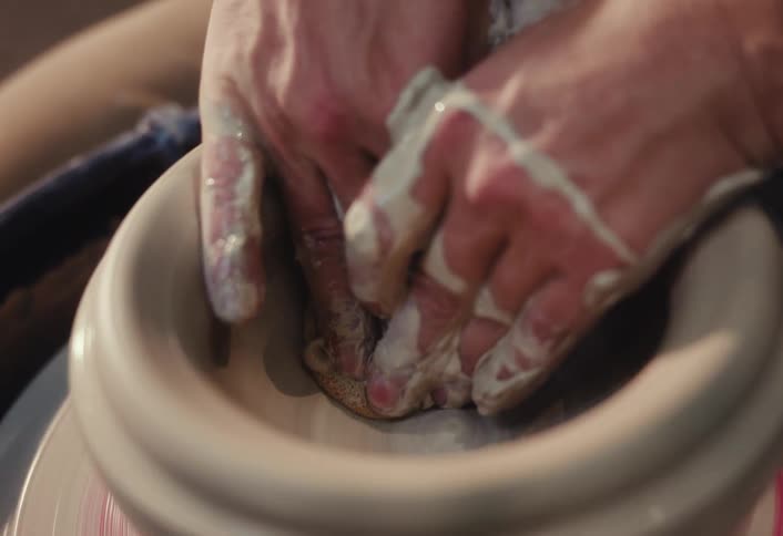 Slow motion close-up of a craftsman's hands carefully shaping the inside of a clay bowl on a spinning potter's wheel