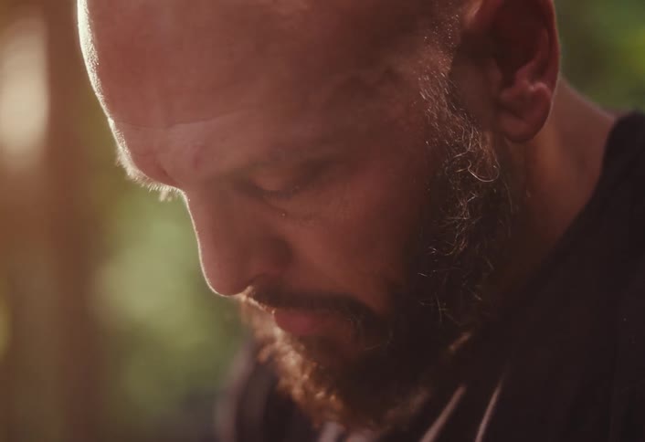 A close-up of a contemplative bearded man looking down, bathed in warm, golden hour sunlight