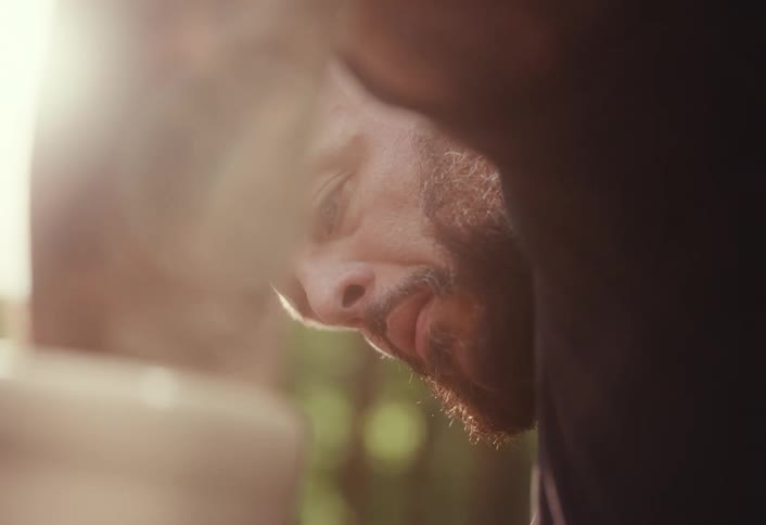An artisan's face is seen in a tight, partially obscured shot as he focuses intensely on his work in a sunlit workshop