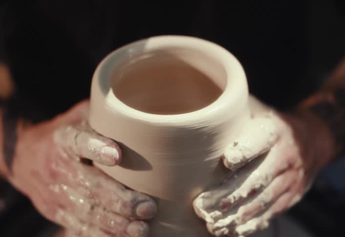 A potter's hands skillfully mold and shape a wet clay pot on a spinning potter's wheel
