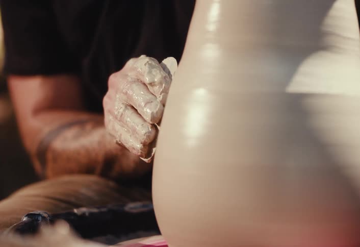 A close-up shot of an artisan's hands carefully shaping a large clay vase on a spinning pottery wheel