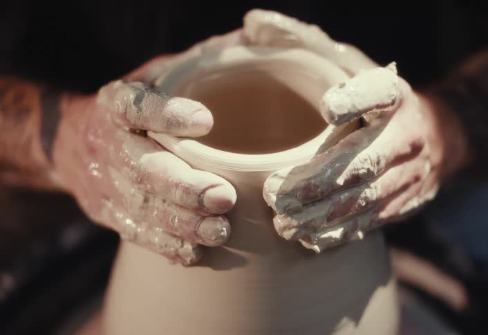 Close up of a craftsman's hands sculpting wet clay into a vessel on a pottery wheel