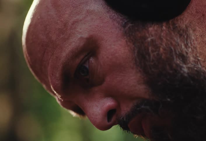 An intense close-up of a serious bald man with a beard looking down thoughtfully