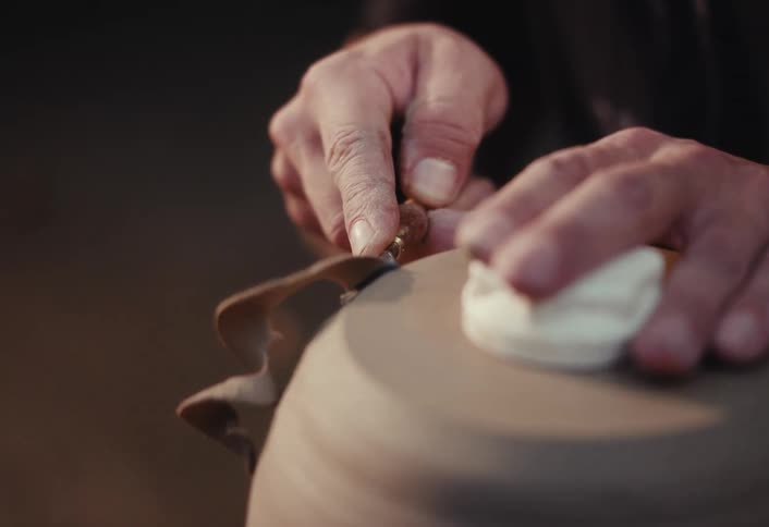 Close-up of a skilled potter meticulously trimming the base of a clay pot on a spinning wheel in slow motion