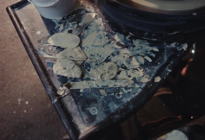 Top-down view of a potter grabbing a tool from a messy clay-splattered tray in their workshop