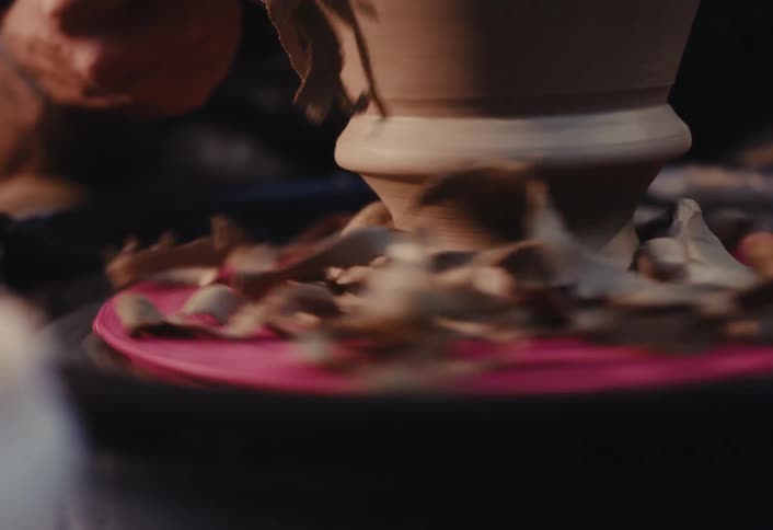 Slow motion close-up of a potter trimming excess clay from the base of a spinning pot on a pottery wheel