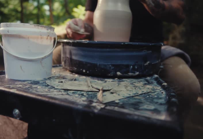Low angle view of a messy pottery wheel station as a potter shapes a clay vase in a sunlit outdoor workshop
