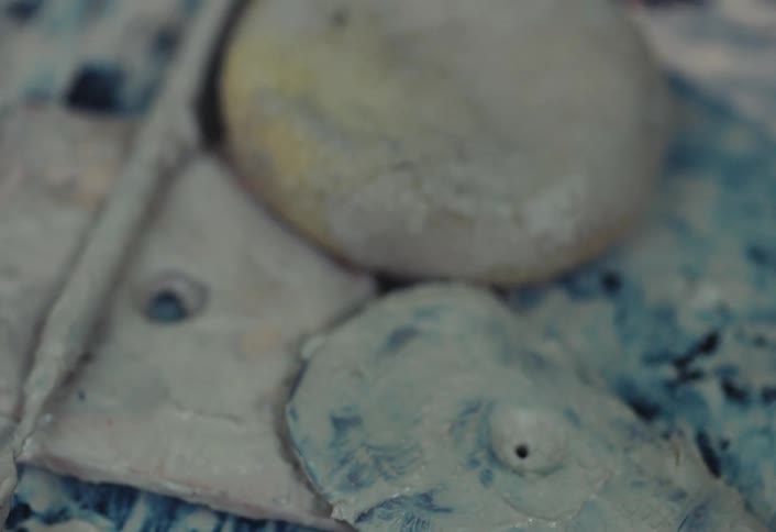 An extreme close-up rack focus shot reveals the intricate textures of a mixed-media abstract art piece