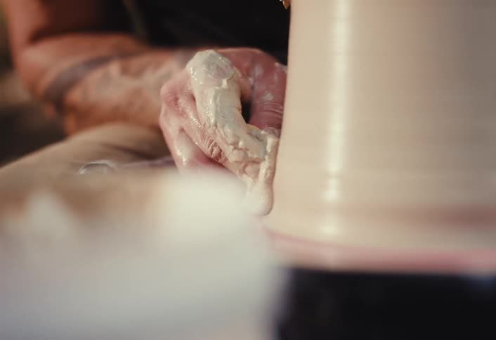 A potter's hands skillfully shape wet clay with a sponge on a spinning pottery wheel in a workshop