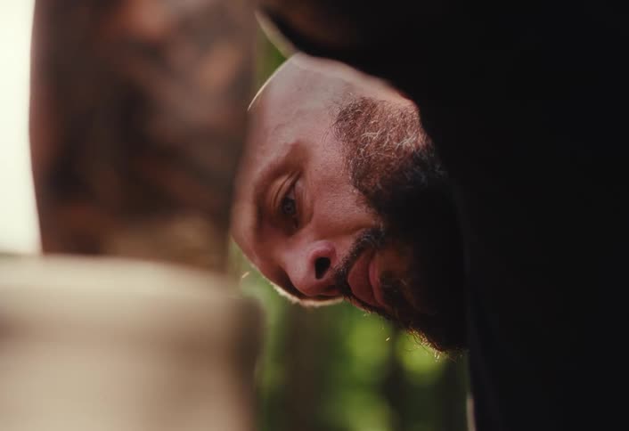 A bald man with a beard leans over to intensely focus on his work in the warm afternoon sun