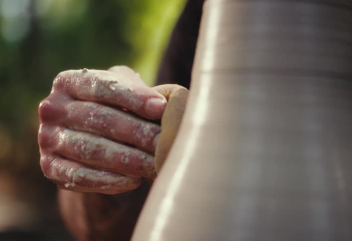An artisan's wet, clay-covered hand delicately shapes a vase with a sponge on a spinning pottery wheel