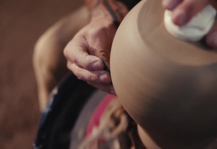Close-up of a potter's hands using tools to meticulously shape a spinning clay pot on a wheel