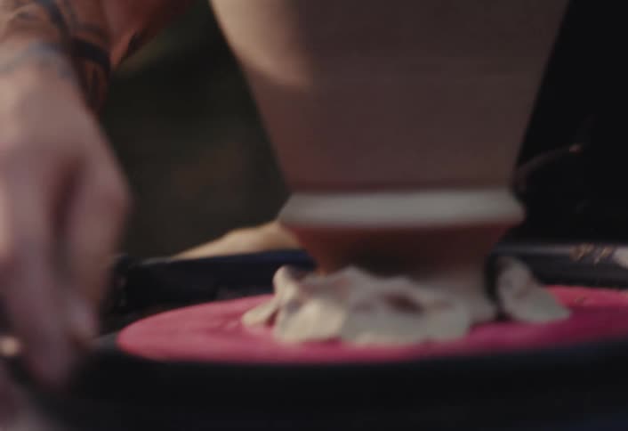 A close-up shot shows a focused, bearded man carefully shaping a clay pot as it spins on a pottery wheel