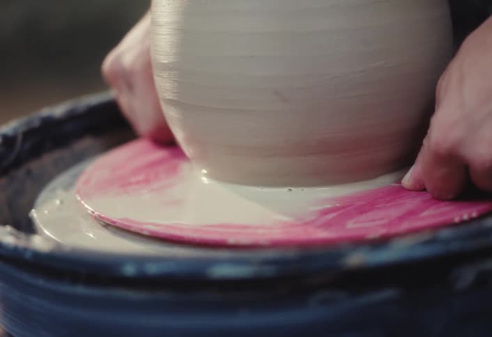 A potter carefully uses a wire tool to remove a finished clay pot from the spinning wheel in slow motion
